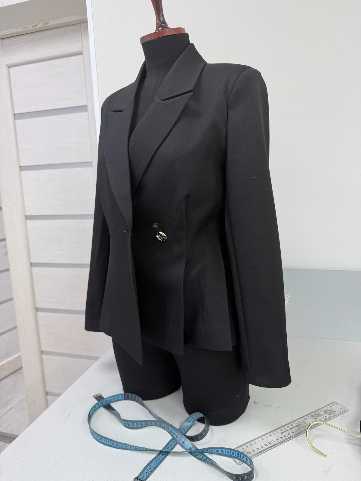 Black tailored blazer on a mannequin with measuring tape in the workshop